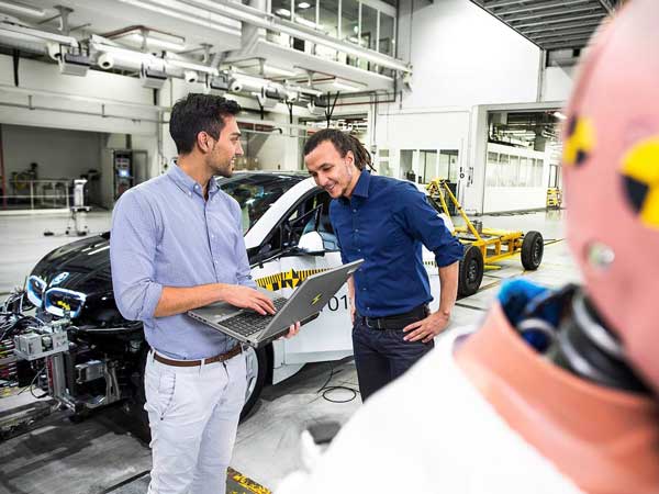 Carmakers for many years have strived to reduce the cost of electric cars. two men discussing over a laptop in an BMW manufacture