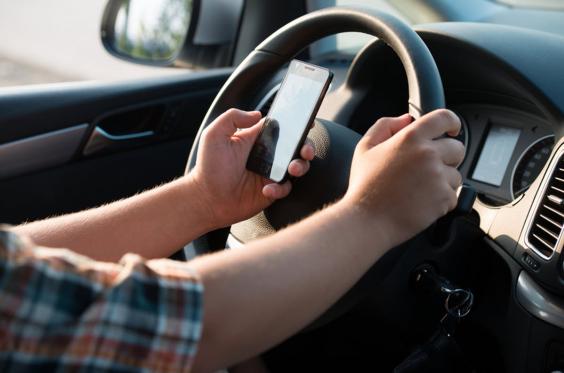 The Do Not Disturb while Driving builds on Apple’s existing Do Not Disturb feature one hand holing steering wheel and one hand using mobile phone