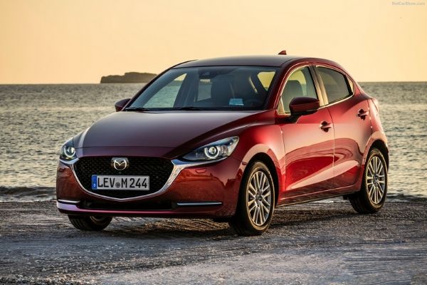 A red Mazda2 by the sea