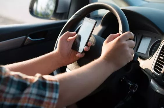 one hand holing steering wheel and one hand using mobile phone