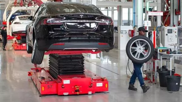 An engineer is carrying a wheel in Tesla automobile assembly plants