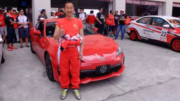 A man posing for a photo in front of a racing car