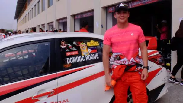 Hot racer standing in front of a racing car and smiling
