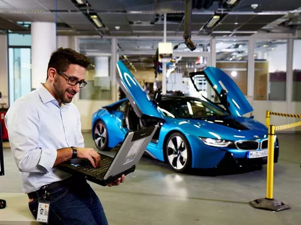 A man using laptop in front of a BMW