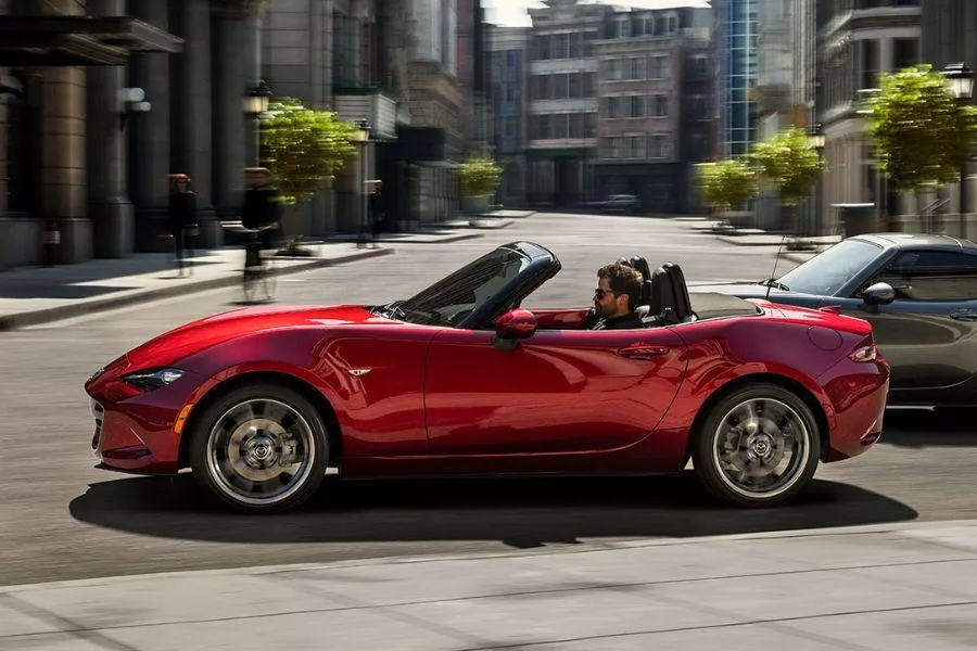 A picture of the side of the MX-5 soft top version as it travels in the city.