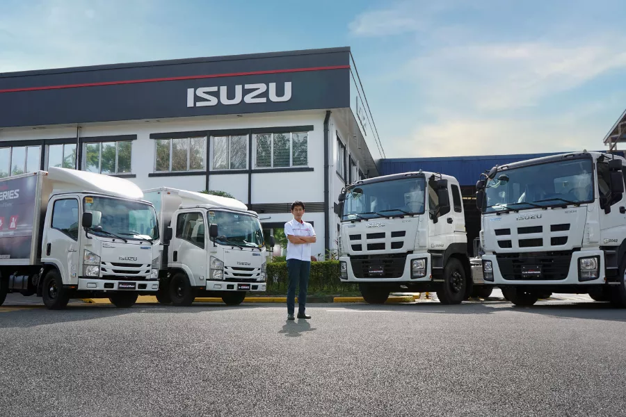 A picture of IPC CEO Noboru Murakami with the Isuzu model lineup of trucks.