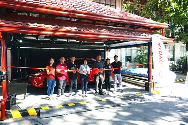 MAPUA students with Toyota representatives with a bright red Toyota Prius C in the background