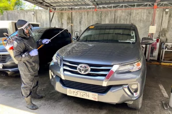 A picture of a Toyota employee disinfecting a parked Toyota Fortuner