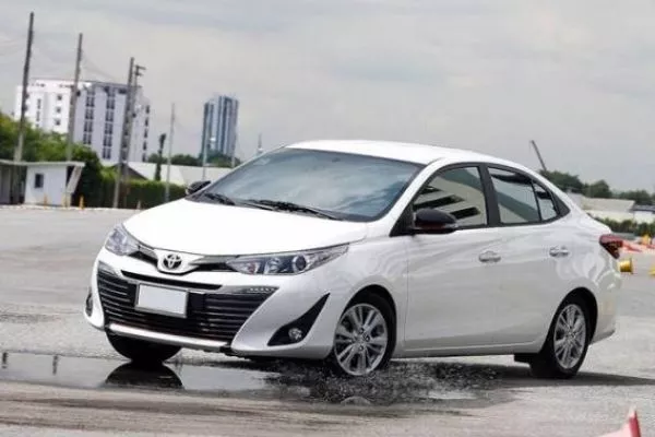 A picture of a white Toyota Vios driving through a park