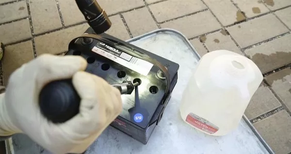 If the car battery needs water, it's preferable to use clean and distilled water Man checking the electrolyte levels of a battery