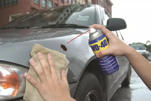 Man spraying WD-40 in the car's finish