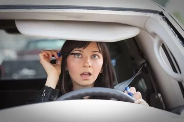 A picture of a young woman putting on makeup while driving