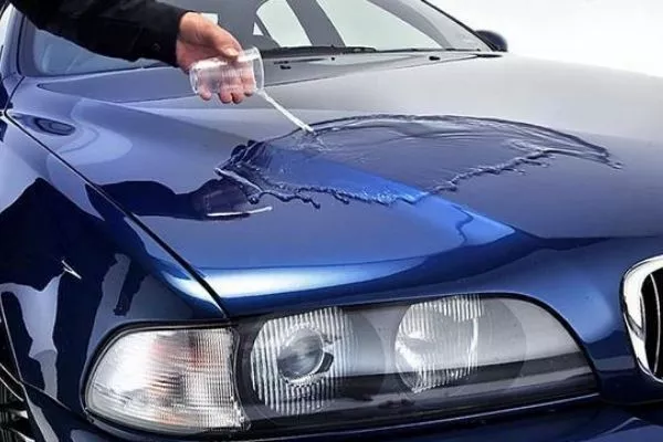 A picture of a man pouring water on a car with glass coating.