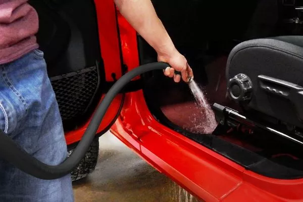 If your Wrangler's interior is full of gunk, remove the carpeting, open the drains, and simply spray away A picture of a man cleaning the Jeep Wrangler interior with a water hose