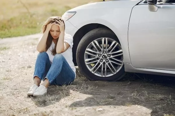 A woman feeling sad beside a car