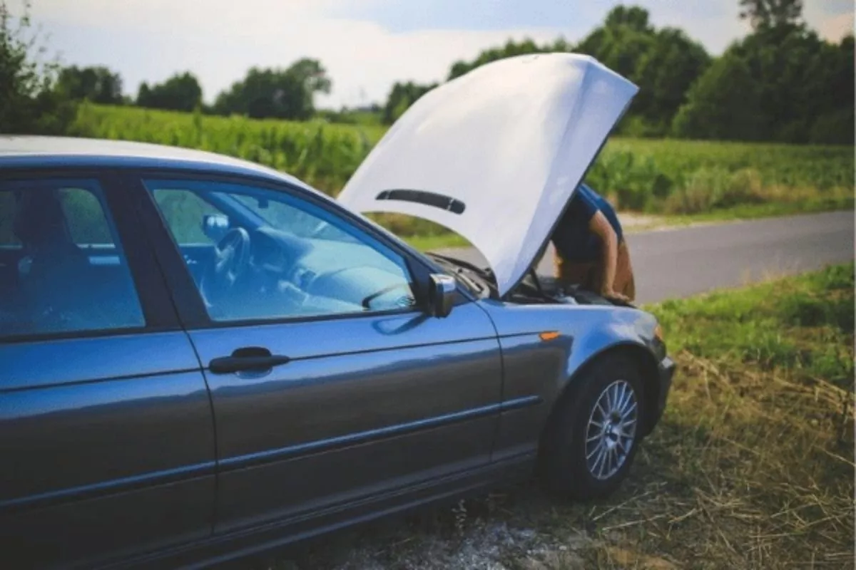 A picture of a man opening his car's hood while stranded on the side of a road.