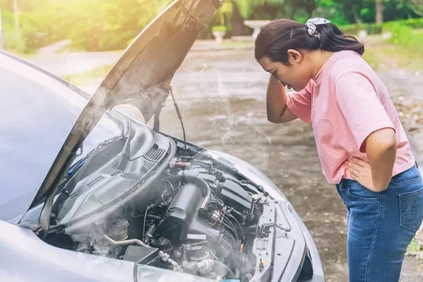 a woman standing in front of an overheated car engine