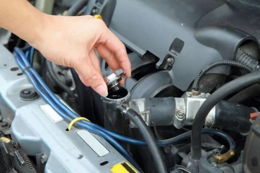 A picture of a person opening a car's radiator cap