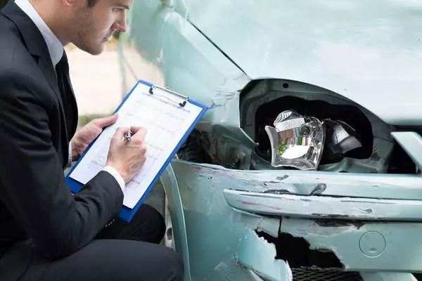 Drive smart and carefully to avoid being labeled by insurance companies as a high-risk driver. insurance agent inspecting a damaged car