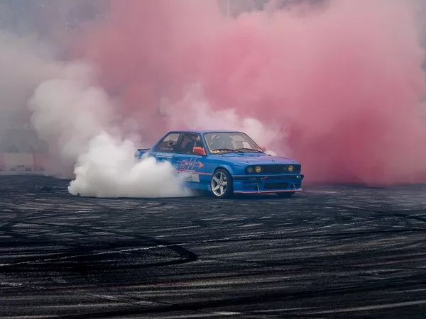 A picture of a BMW drift car doing burnouts with red colored tire smoke
