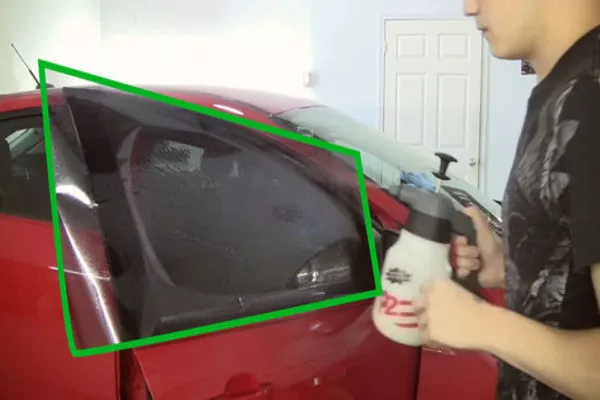 Using more soapy water, spray the part of the tint exposed to you Man spraying the car tint
