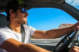 A man wearing glasses driving a car 