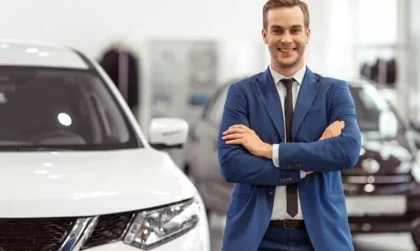 A well-dressed up salesman standing beside a car