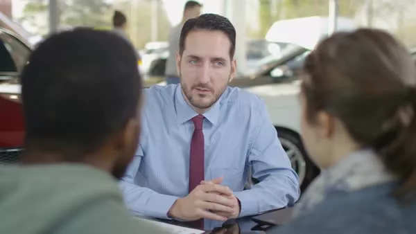 A car salesman is talking in front of two customers