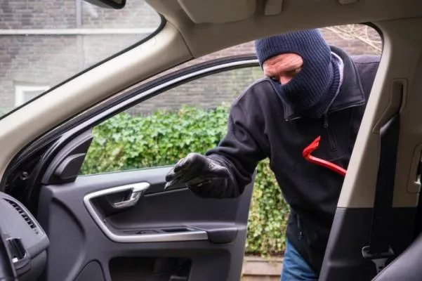 a man wearing mask breaking into a car